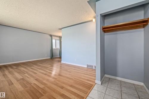 Entryway featuring a built-in wooden shelf and tile flooring, opening into a spacious room with wood-finish flooring, light blue walls, and a window with natural light - 13320 123 Street Nw, Edmonton, AB - Indoor Photo Showing Other Room
