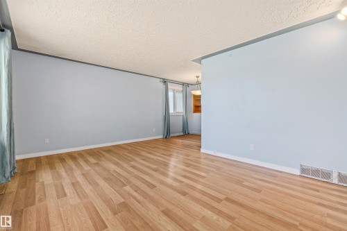 Spacious interior featuring wood-finish flooring, light blue walls, white baseboards, and a textured ceiling - 13320 123 Street Nw, Edmonton, AB - Indoor Photo Showing Other Room