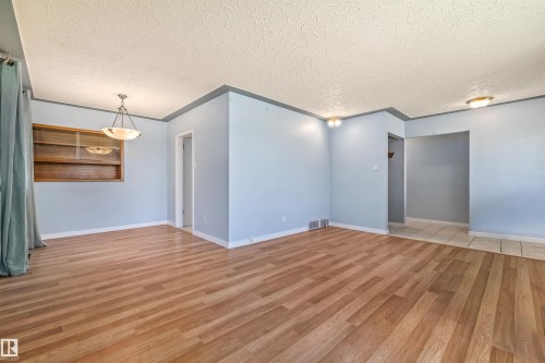 Spacious room featuring wood-finish flooring, a built-in wooden display cabinet, and a multi-light pendant fixture - 13320 123 Street Nw, Edmonton, AB - Indoor Photo Showing Other Room