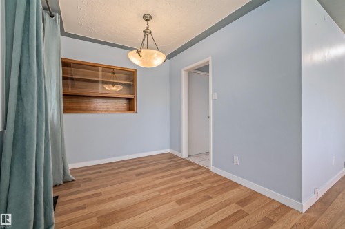 Interior space featuring wood-finish flooring, a built-in wooden display cabinet, and a decorative pendant light fixture - 13320 123 Street Nw, Edmonton, AB - Indoor Photo Showing Other Room