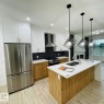 Kitchen featuring stainless steel appliances, white cabinetry, wood-finish base cabinets, a dark hexagonal tile backsplash, and an island with a double sink and white countertop - 12909 69 Street Nw, Edmonton, AB 