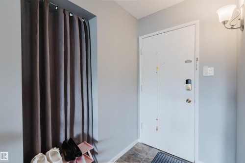 Recessed entryway with a white door, wall-mounted sconce lighting, and tiled flooring - #126 5125 Riverbend Rd Nw, Edmonton, AB 