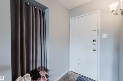 Recessed entryway with a white door, wall-mounted sconce lighting, and tiled flooring - 