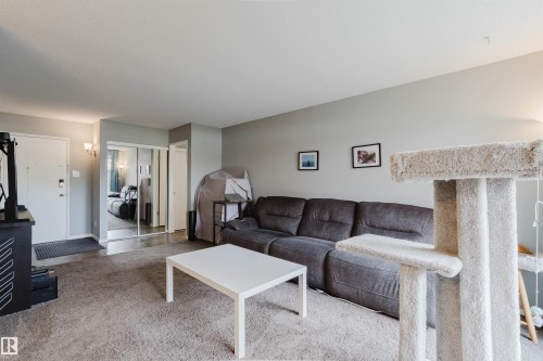 Carpeted living area with light gray walls, white entry door, and mirrored closet doors - #126 5125 Riverbend Rd Nw, Edmonton, AB 