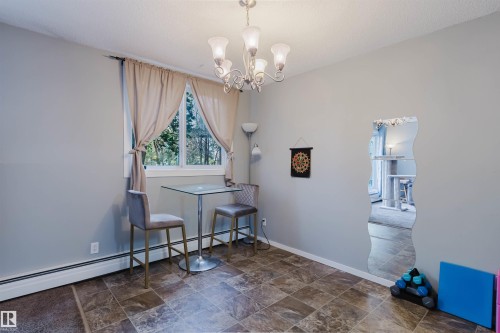 Recessed window with exterior foliage, tile-patterned flooring, light-toned walls, and a multi-bulb chandelier - #126 5125 Riverbend Rd Nw, Edmonton, AB 