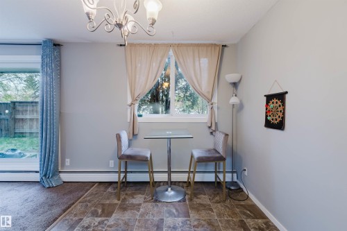 Sliding glass door, chandelier lighting, window with trim, tile flooring, and light-colored wall paint - #126 5125 Riverbend Rd Nw, Edmonton, AB 