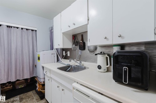 White cabinetry with brushed nickel hardware, light-toned countertop, stainless steel sink, and gray textured backsplash - #126 5125 Riverbend Rd Nw, Edmonton, AB 