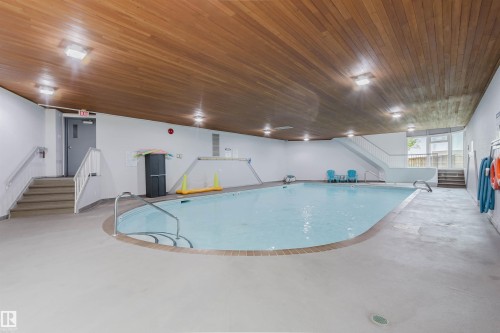 Indoor swimming pool featuring a wood-finish ceiling, integrated overhead lighting, and two sets of stairs with railings - #126 5125 Riverbend Rd Nw, Edmonton, AB 