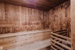 Wood-paneled sauna featuring built-in wooden benches and an integrated heater with a protective wood enclosure - 