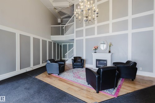 Two-story ceiling, gas fireplace, wood-finish flooring, staircase with white railing, and a decorative chandelier - #126 5125 Riverbend Rd Nw, Edmonton, AB 
