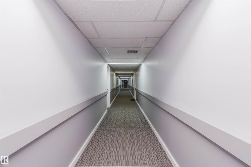 Long corridor featuring drop ceiling, recessed lighting, and patterned carpeting - #126 5125 Riverbend Rd Nw, Edmonton, AB 