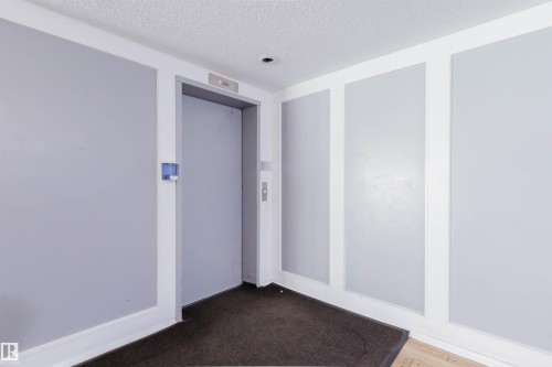 Elevator access with a textured ceiling, recessed lighting, and wall paneling - #126 5125 Riverbend Rd Nw, Edmonton, AB 