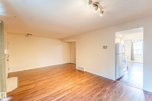 Wood-finish flooring throughout, track lighting, and a white brick fireplace with a built-in mantel - #4 3221 119 St Nw, Edmonton, AB 