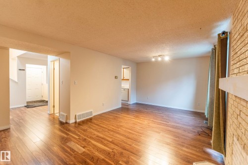Wood-finish flooring, white painted walls, brick-finish accent wall with white mantel, track lighting fixture, and a white paneled door - #4 3221 119 St Nw, Edmonton, AB 