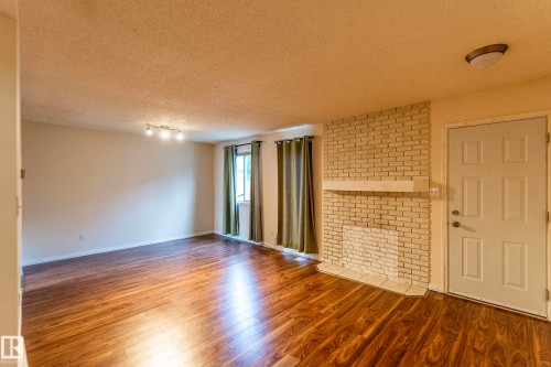 Wood-finish flooring, white painted brick fireplace with hearth, track lighting, and a paneled entry door - #4 3221 119 St Nw, Edmonton, AB 