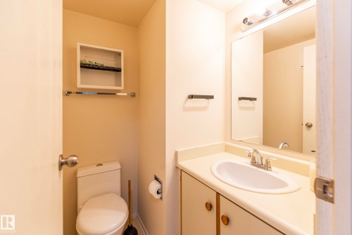 Vanity with an integrated sink and chrome faucet, large wall mirror, and overhead vanity lighting - #4 3221 119 St Nw, Edmonton, AB 