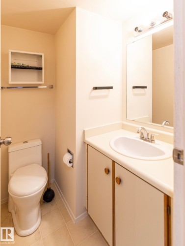 White vanity with wood-tone trim and circular cabinet pulls, featuring an integrated sink, polished chrome faucet, and a wall-mounted mirror with overhead light fixture - #4 3221 119 St Nw, Edmonton, AB 