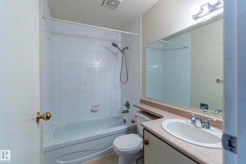 Bathroom featuring a bathtub with shower, white tile surround, vanity with integrated sink, and an overhead light fixture - #4 3221 119 St Nw, Edmonton, AB 