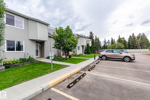 Exterior featuring light-colored siding, a covered entrance, a concrete walkway, and a manicured lawn - #4 3221 119 St Nw, Edmonton, AB 