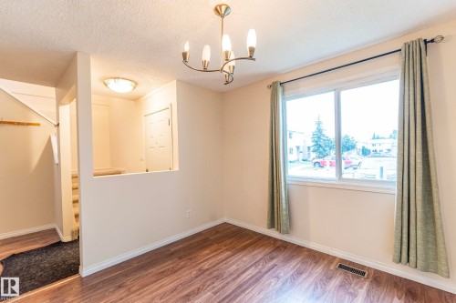 Wood-finish flooring, a contemporary chandelier, and a large window providing natural light - #4 3221 119 St Nw, Edmonton, AB 