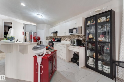 Kitchen featuring white cabinetry, light-toned countertops, mosaic tile backsplash, built-in microwave, and stainless steel refrigerator - 3519 22 Street Nw, Edmonton, AB 
