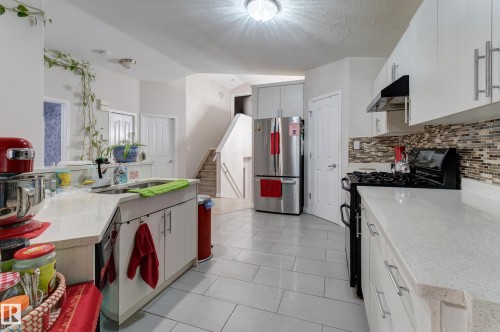 Kitchen featuring white cabinetry, light-toned countertops, a full-size stainless steel refrigerator, a black gas range, and a mosaic tile backsplash - 3519 22 Street Nw, Edmonton, AB 