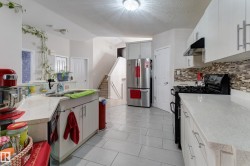 Kitchen featuring white cabinetry, light-toned countertops, a full-size stainless steel refrigerator, a black gas range, and a mosaic tile backsplash - 