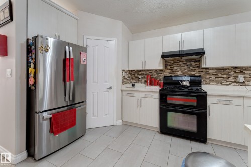 Stainless steel refrigerator, white cabinetry, integrated range hood, mosaic tile backsplash, and light-toned tile flooring - 3519 22 Street Nw, Edmonton, AB 