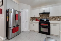 Stainless steel refrigerator, white cabinetry, integrated range hood, mosaic tile backsplash, and light-toned tile flooring - 