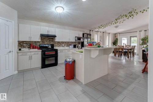 Kitchen featuring white cabinetry, a dark appliance package, a tile backsplash, and light-toned tile flooring - 3519 22 Street Nw, Edmonton, AB 