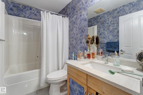 White integrated tub and shower unit, wood-finish vanity with a light countertop, integrated sink, and an expansive wall-mounted mirror - 3519 22 Street Nw, Edmonton, AB 