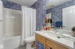 White integrated tub and shower unit, wood-finish vanity with a light countertop, integrated sink, and an expansive wall-mounted mirror - 