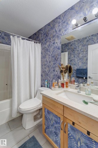 Bathroom featuring a built-in bathtub with shower, a vanity with a white countertop and integrated sink, a wall-mounted mirror, and patterned wall covering - 3519 22 Street Nw, Edmonton, AB 