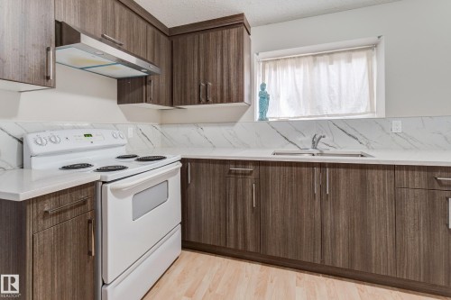 Wood-finish cabinetry, light-toned countertops, white range, stainless steel range hood, and a stainless steel sink - 3519 22 Street Nw, Edmonton, AB 