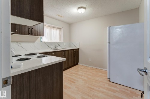Kitchen featuring wood-finish cabinetry, white countertops with integrated sink, white refrigerator, and wood-finish flooring - 3519 22 Street Nw, Edmonton, AB 
