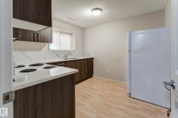 Kitchen featuring wood-finish cabinetry, white countertops with integrated sink, white refrigerator, and wood-finish flooring - 