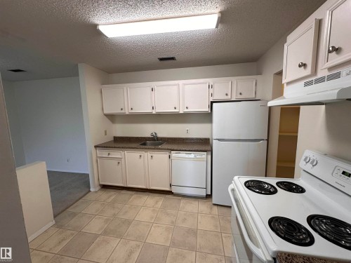 Kitchen featuring white cabinetry, a built-in dishwasher, white electric range, and tiled flooring - #132 2703 79 St Nw, Edmonton, AB 