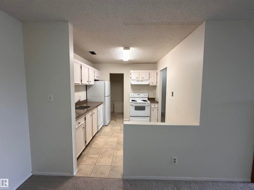 Kitchen featuring white cabinetry, white appliances, speckled countertops, and tile flooring - #132 2703 79 St Nw, Edmonton, AB 