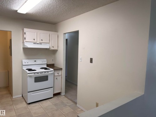 Kitchenette featuring white cabinetry, a white electric range, and a light-toned tile floor - #132 2703 79 St Nw, Edmonton, AB 