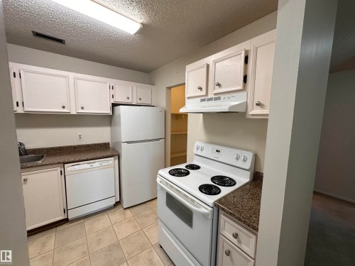 Kitchen featuring white cabinetry, solid surface countertops, tile flooring, and white appliances including a range, refrigerator, and dishwasher - #132 2703 79 St Nw, Edmonton, AB 