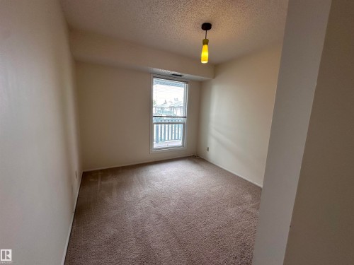 Soft brown carpeting, neutral wall tones, window with vertical blinds, and a modern pendant light fixture - #132 2703 79 St Nw, Edmonton, AB 