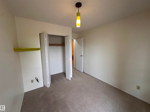 Neutral wall paint with carpet flooring, featuring a built-in closet with bi-fold doors and a ceiling-mounted pendant light fixture - #132 2703 79 St Nw, Edmonton, AB 