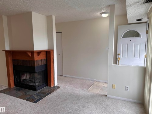 Living space with a wood-mantel fireplace featuring a brick surround and slate tile hearth - #132 2703 79 St Nw, Edmonton, AB 