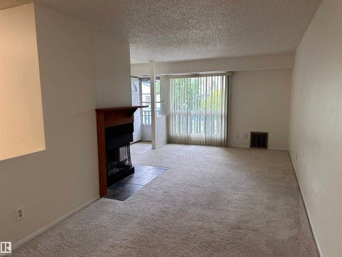 Carpeted living area featuring a fireplace with a wood-finish mantel and a tiled hearth - #132 2703 79 St Nw, Edmonton, AB 