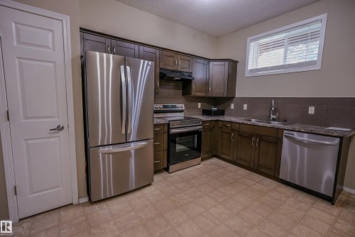 Kitchen featuring dark wood-finish cabinetry, stainless steel appliances, patterned countertop, and tile flooring - 122 142 Selkirk Place, Leduc, AB 