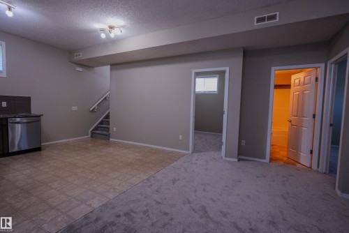 Stainless steel dishwasher, dark cabinetry with stone-finish countertop, track lighting, and two-tone flooring - 122 142 Selkirk Place, Leduc, AB 
