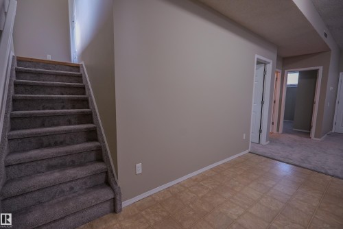 Carpeted staircase with white risers, neutral wall paint, tile flooring, and white trim - 122 142 Selkirk Place, Leduc, AB 