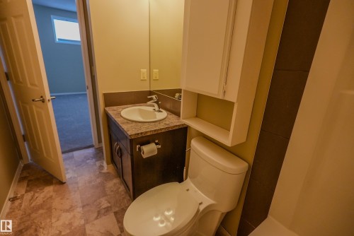Bathroom featuring a wood-finish vanity with a built-in sink, a wall-mounted mirror, a white toilet, and a white storage cabinet with an open shelf - 122 142 Selkirk Place, Leduc, AB 