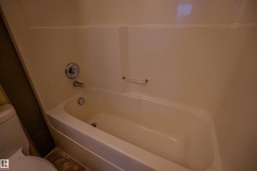 White bathtub with integrated shower surround, chrome fixtures, and a grab bar - 122 142 Selkirk Place, Leduc, AB 