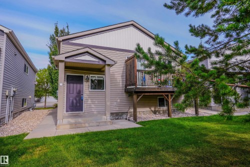 Exterior featuring light-colored siding, a covered entry, an elevated wood-finish deck with a privacy screen, and a concrete walkway - 122 142 Selkirk Place, Leduc, AB 